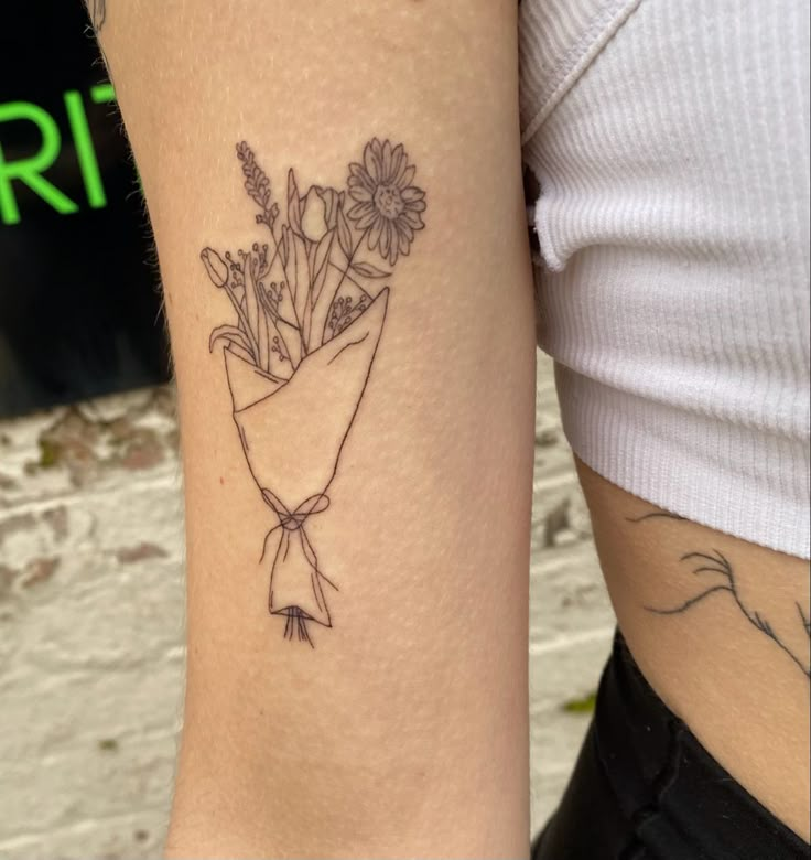 a woman with a tattoo on her arm has a bouquet of flowers wrapped in a ribbon