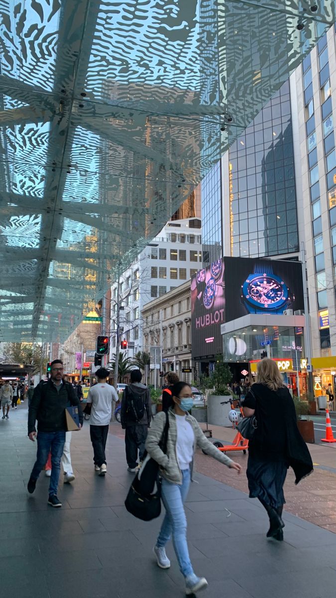 many people are walking on the sidewalk in front of buildings and glass coverings over them