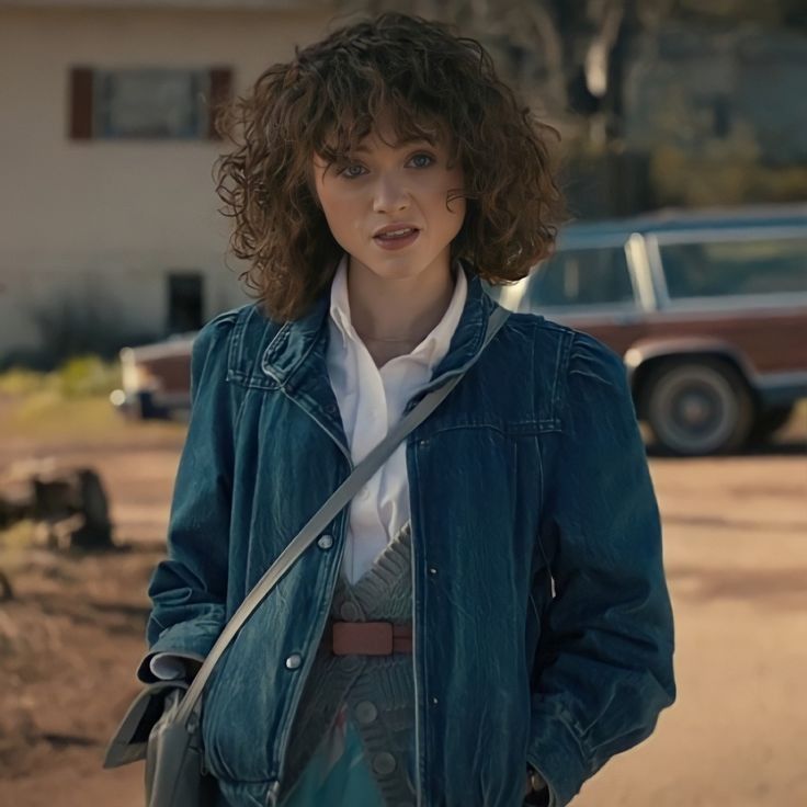 a woman standing in front of a house with her hands on her hips and looking at the camera