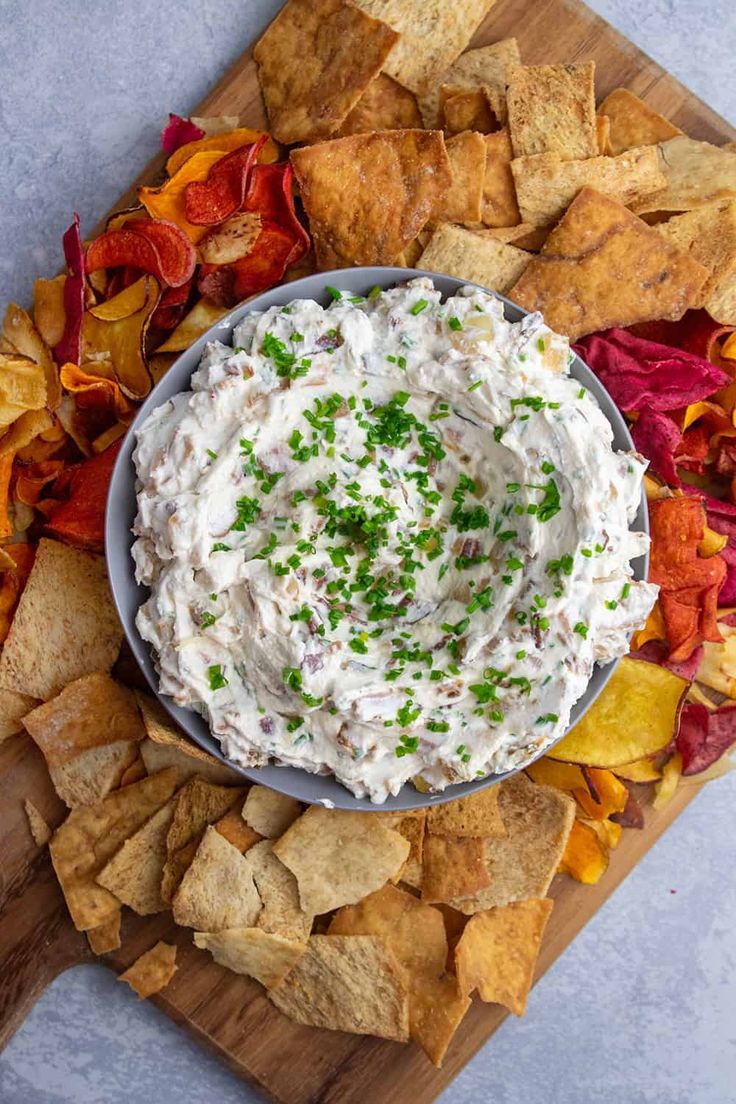 a bowl of dip surrounded by chips on a cutting board