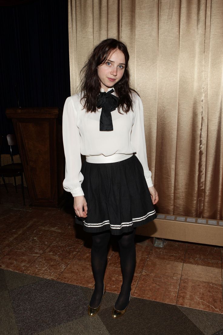 a woman in a white shirt and black skirt standing next to a window with curtains