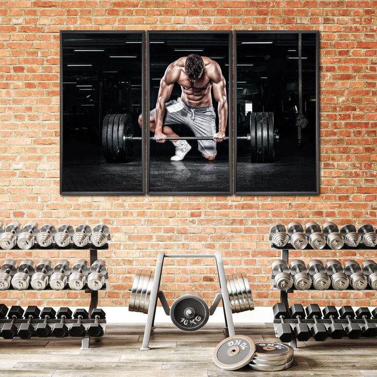 a man doing squats with dumbbells in front of a brick wall and gym equipment