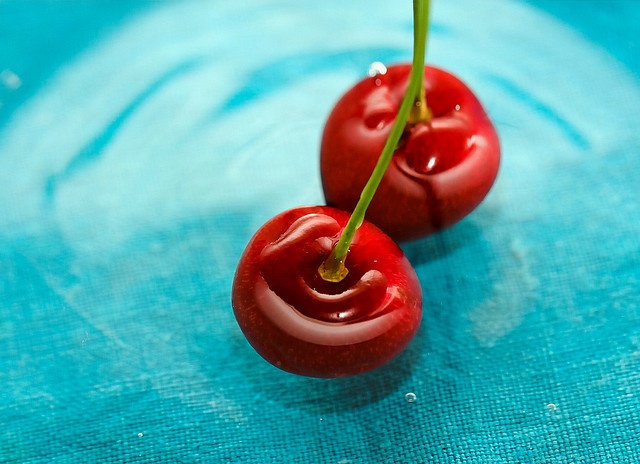 two red cherries sitting on top of a blue cloth