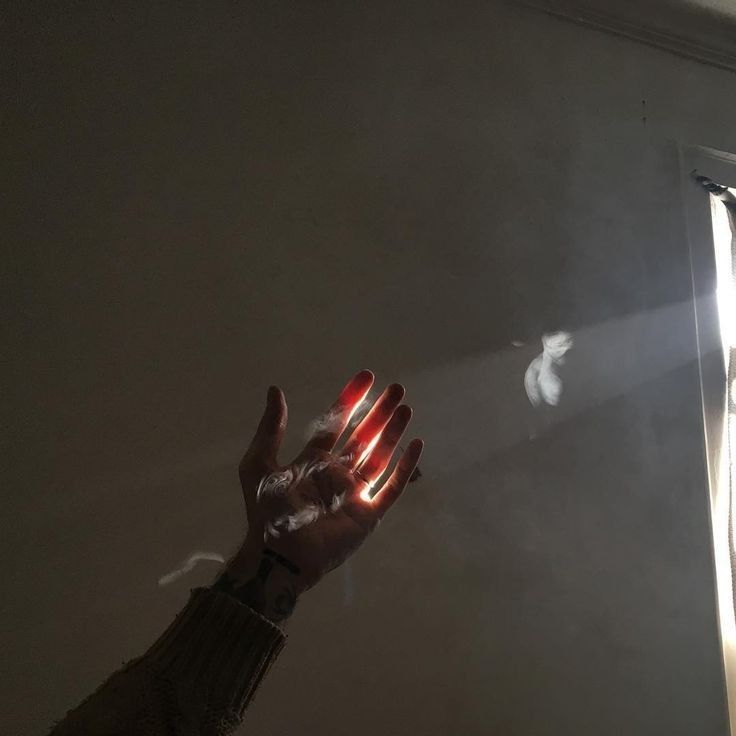 a person's hand reaching up towards the light coming in from behind an open window