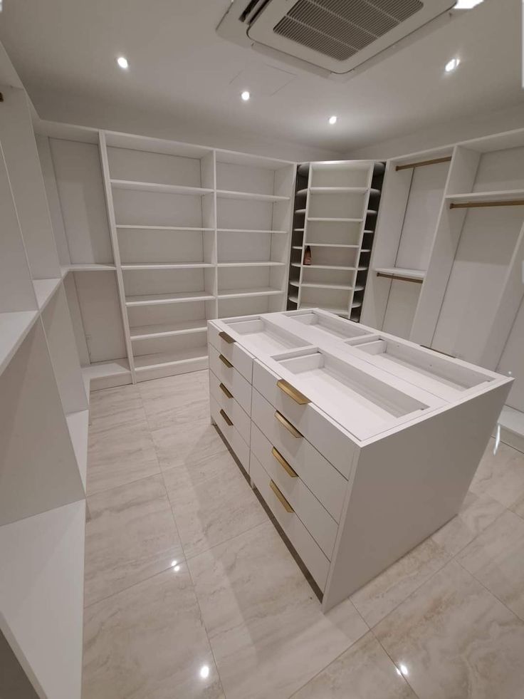 an empty walk in closet with white cabinets and shelves on the wall, along with marble flooring