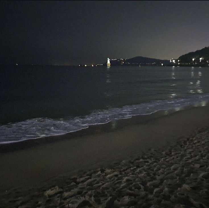 the beach at night with waves coming in from the water and buildings on the horizon