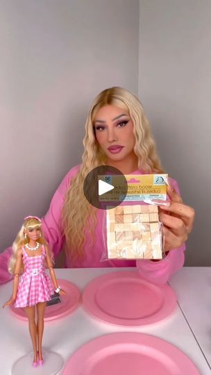 a barbie doll is holding up a package of food in front of a table with pink plates