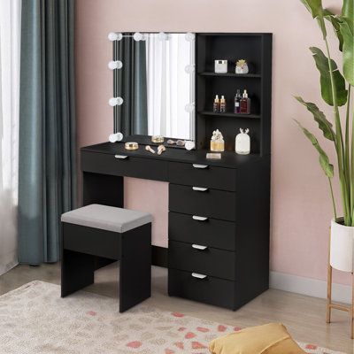 a black vanity with mirror and stool in front of a pink wall, next to a potted plant