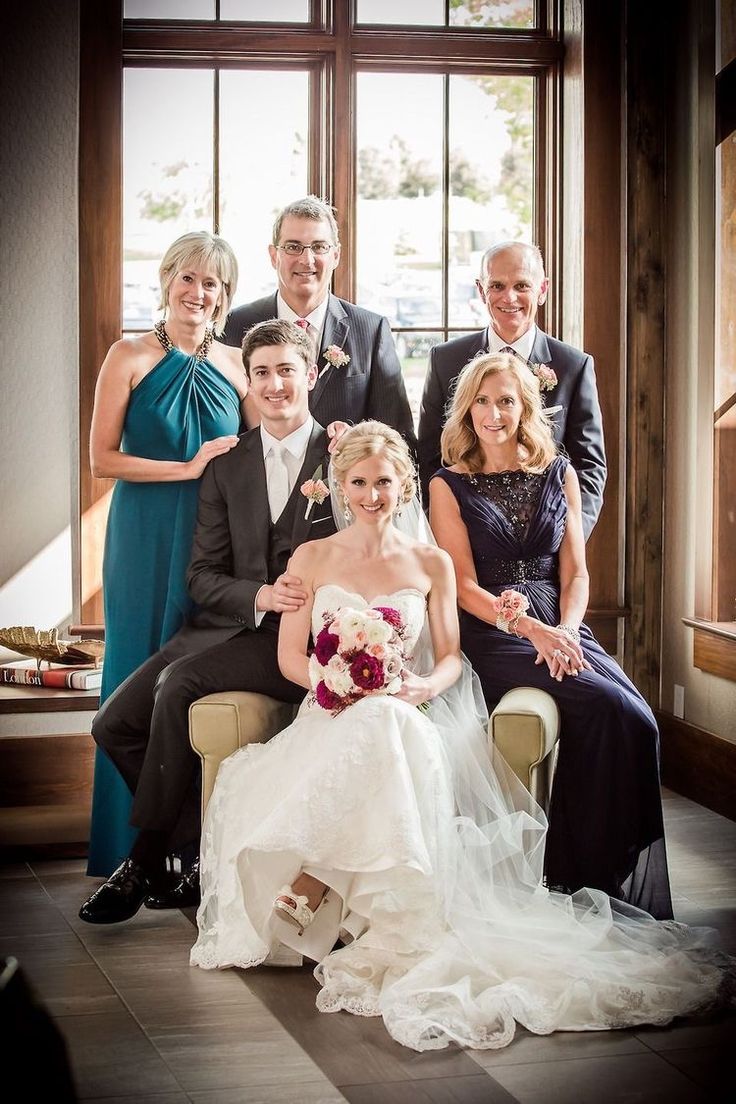 a bride and groom with their family posing for a photo in front of a window