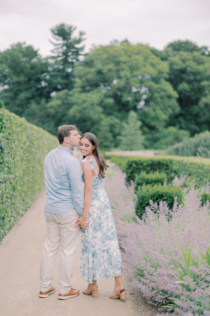 an engaged couple standing next to each other on a path surrounded by lavender bushes and trees