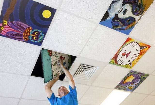 a man is reaching up to paint on the ceiling in an art room with paintings