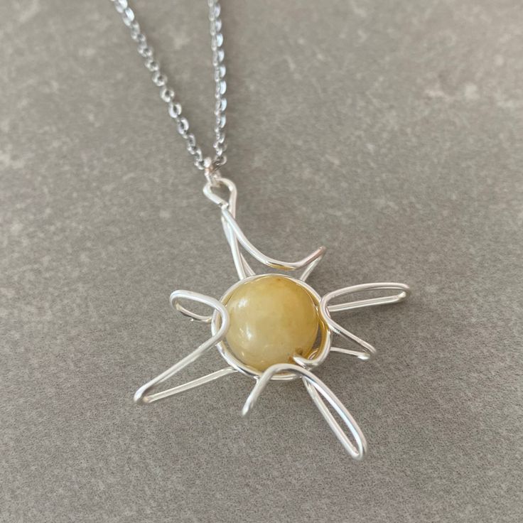 a silver necklace with a yellow stone in the center on a gray surface, it is attached to a chain