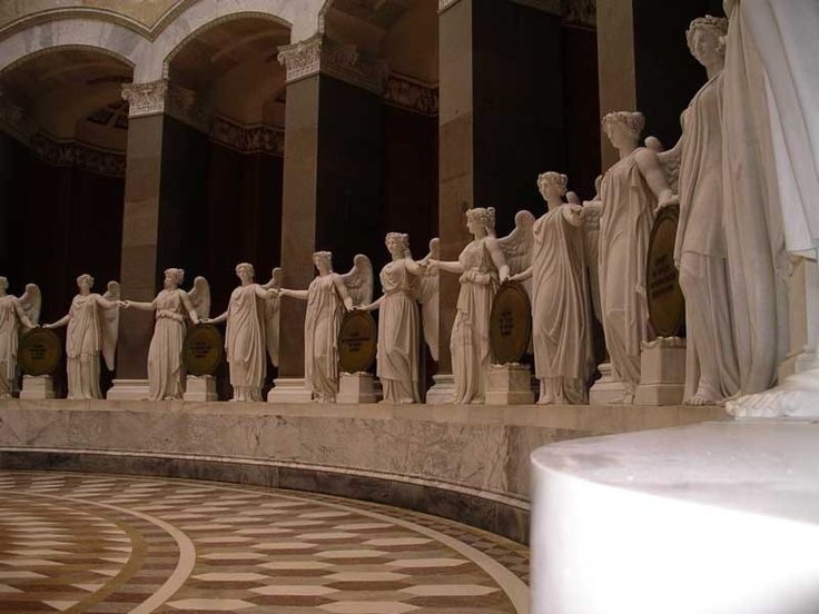 the statues are all lined up on the marble floor in front of columns and arches