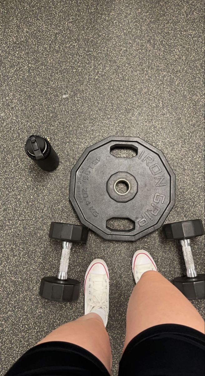 a person standing in front of a weight plate and dumbbells on the ground