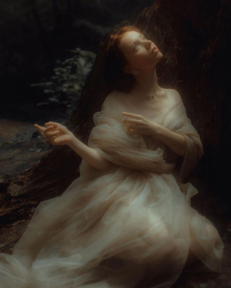 a woman in a white dress sitting next to a tree