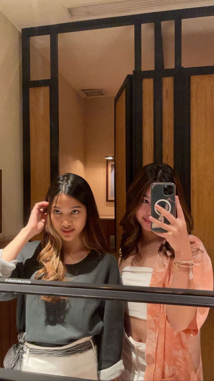 two young women taking a selfie in front of a mirror while standing next to each other