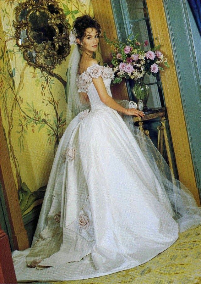 a woman in a white wedding dress standing next to a mirror with flowers on it