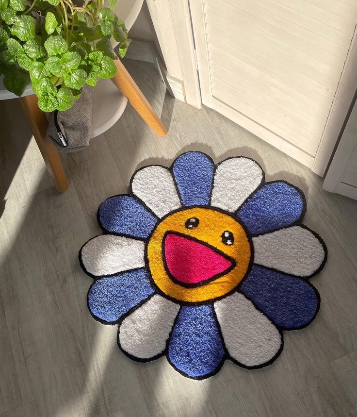 a blue and white flower rug with a smiling face on the floor next to a potted plant