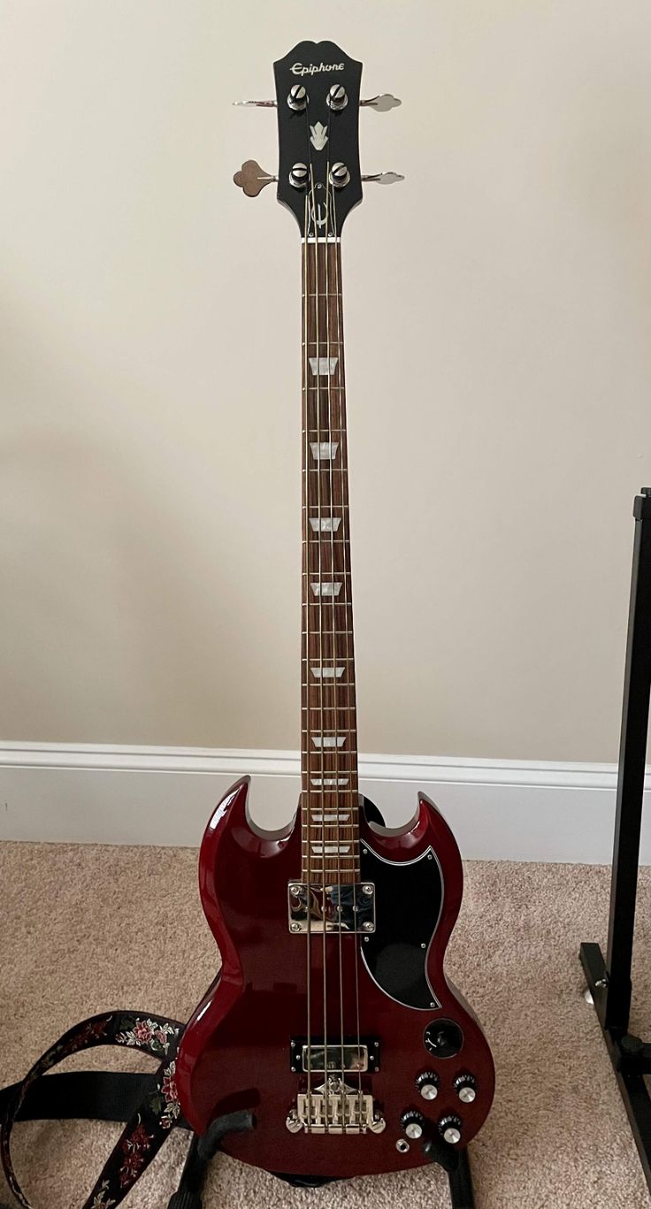 a red guitar sitting on top of a carpeted floor next to a black stand