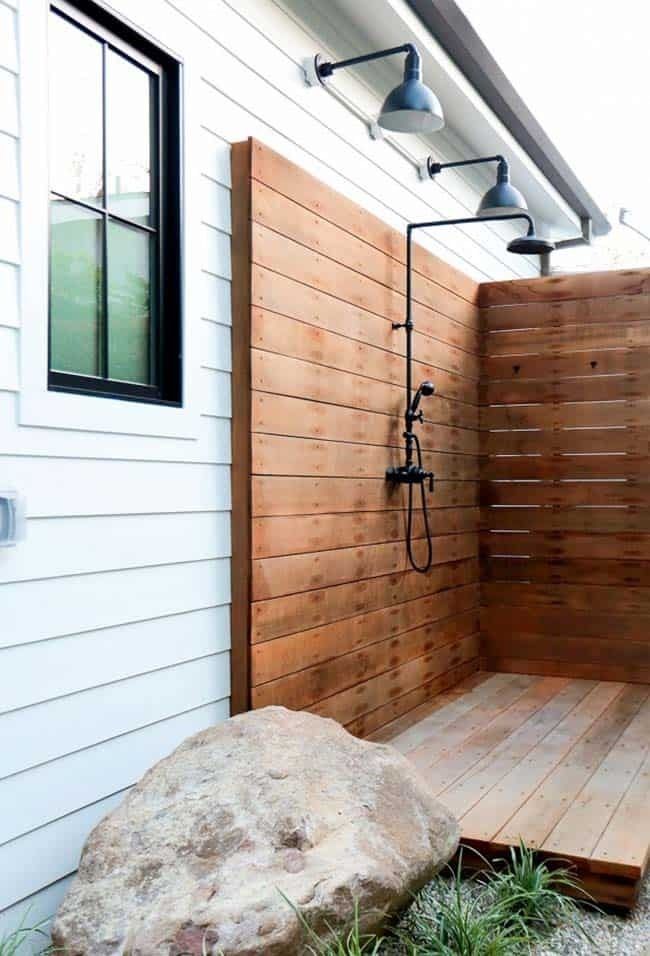 an outdoor shower with wooden planks next to a rock and planter on the side of a house