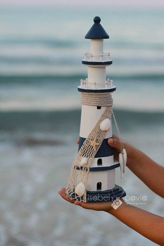 a hand holding a small lighthouse made out of rope and buoys on the beach