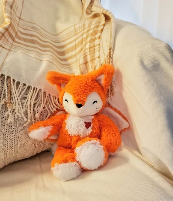 an orange stuffed animal sitting on top of a bed next to a white and beige pillow