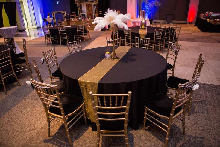 an empty banquet room with black and gold table cloths, white feather centerpieces and chairs