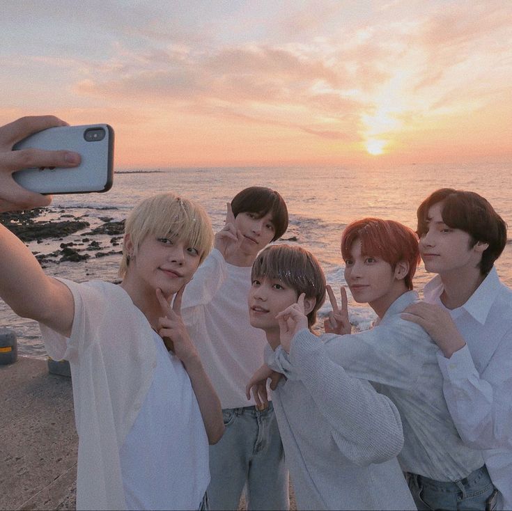 group of young men taking selfie with cell phone at sunset by the water's edge