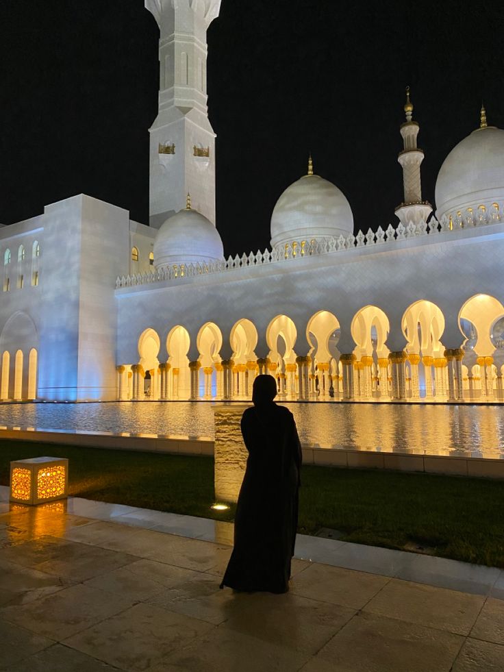 a person standing in front of a white building at night with lights on the walls