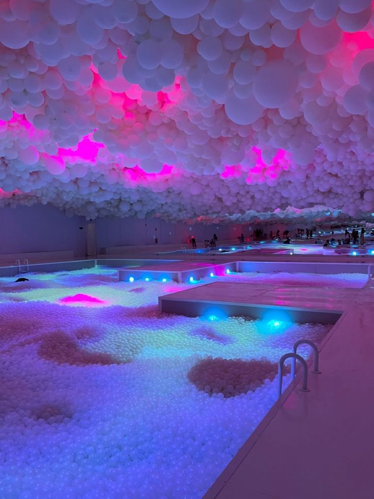 an indoor swimming pool is lit up with colorful lights and balloons hanging from the ceiling