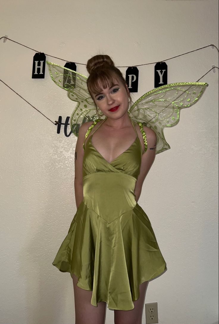 a woman dressed as tinkerbell standing in front of a happy birthday sign on the wall