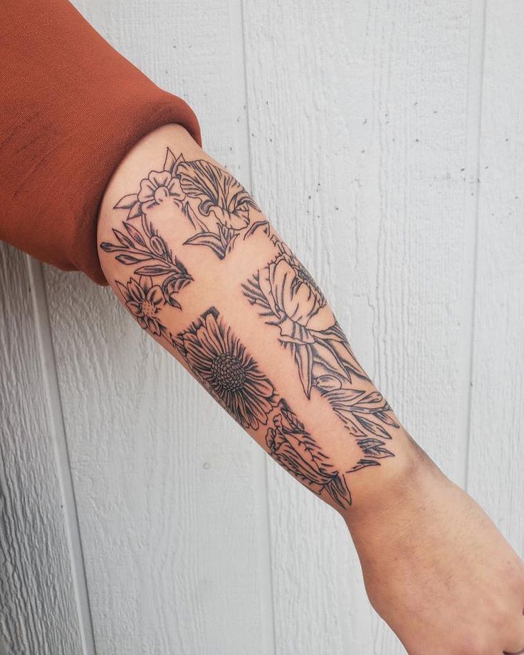 a person's arm with tattoos on it and flowers in the middle, sitting against a white wall