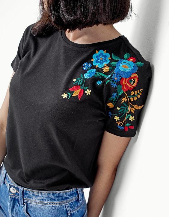 a woman is leaning against a wall with her back to the camera, wearing jeans and a black t - shirt with colorful flowers on it