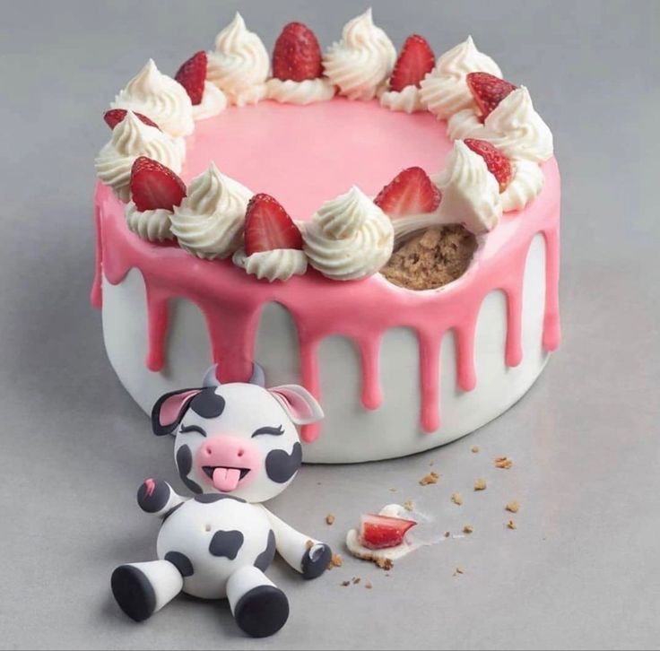 a cake with white icing and strawberries on top next to a small toy cow