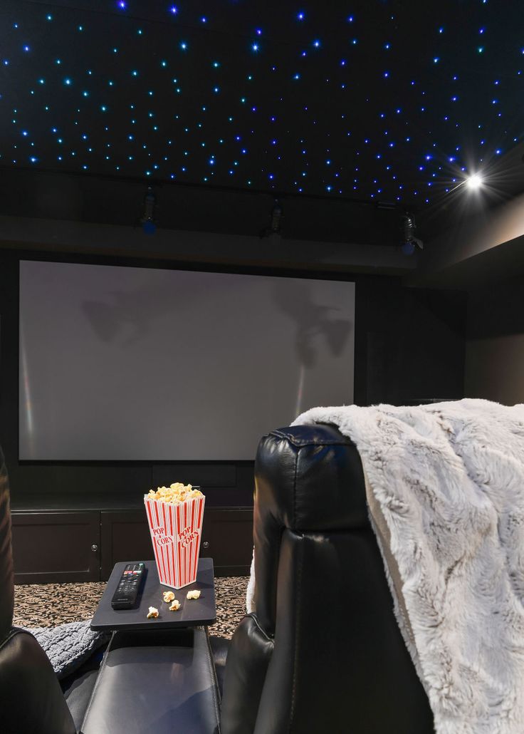 an empty theater room with two recliners and a large screen