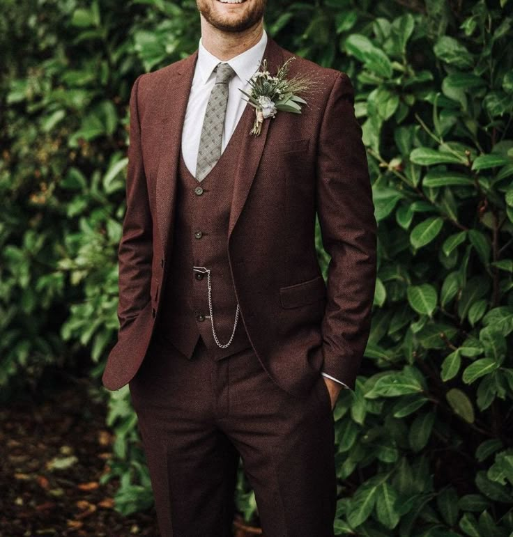 a man wearing a suit and tie standing in front of some bushes smiling at the camera