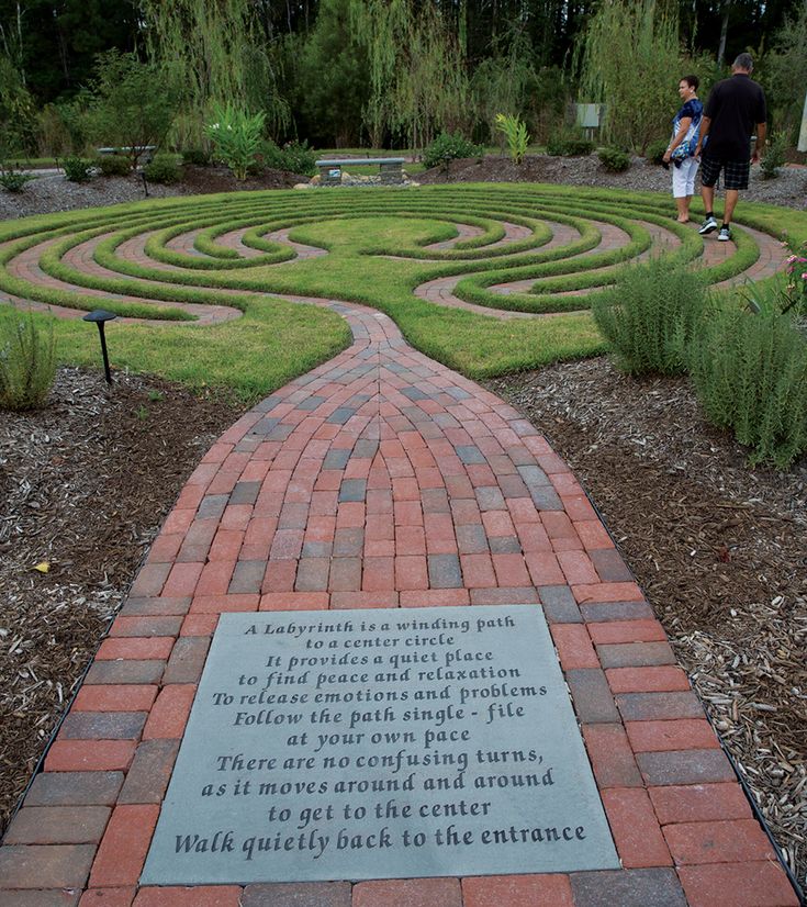 a brick path leads to a maze in the middle of a garden with people walking around it