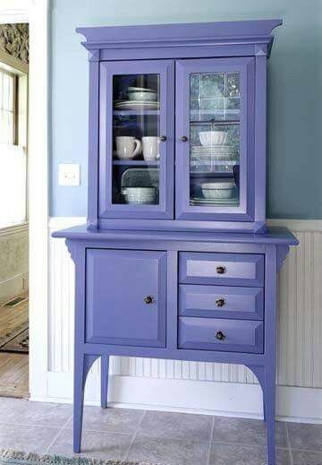 a purple china cabinet with glass doors and drawers in a blue dining room, next to a white wall