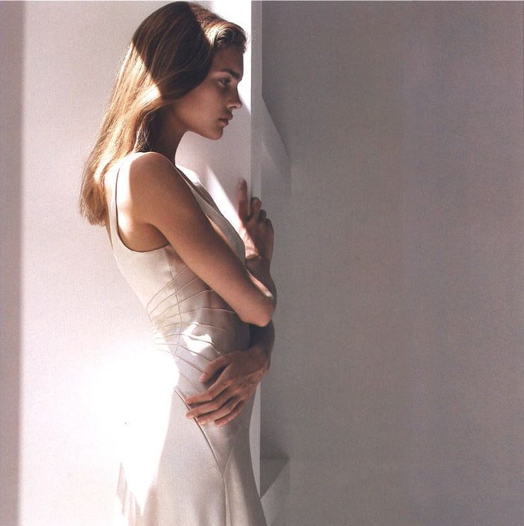 a woman in a white dress leaning against a wall