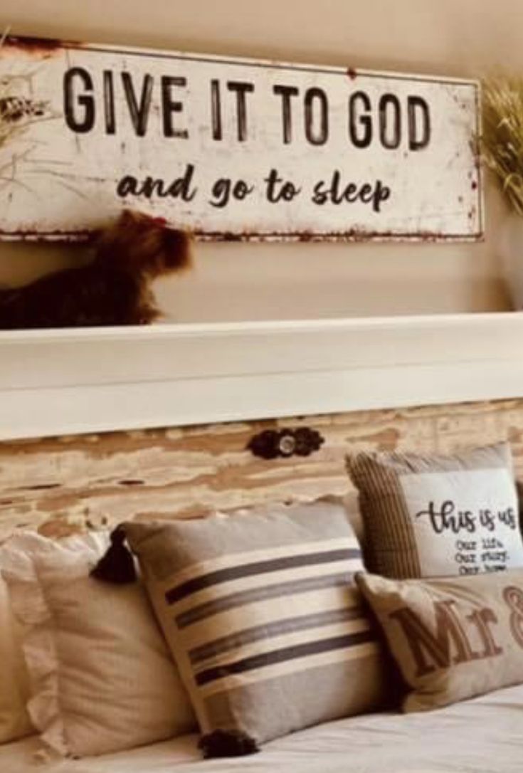 a bed topped with lots of pillows next to a wooden sign that says give it to god and go to sleep