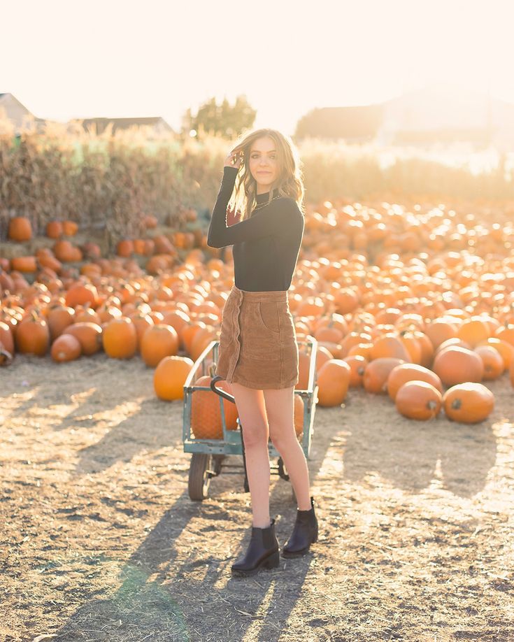 a woman standing in front of pumpkins with her hand on her head and looking at the camera