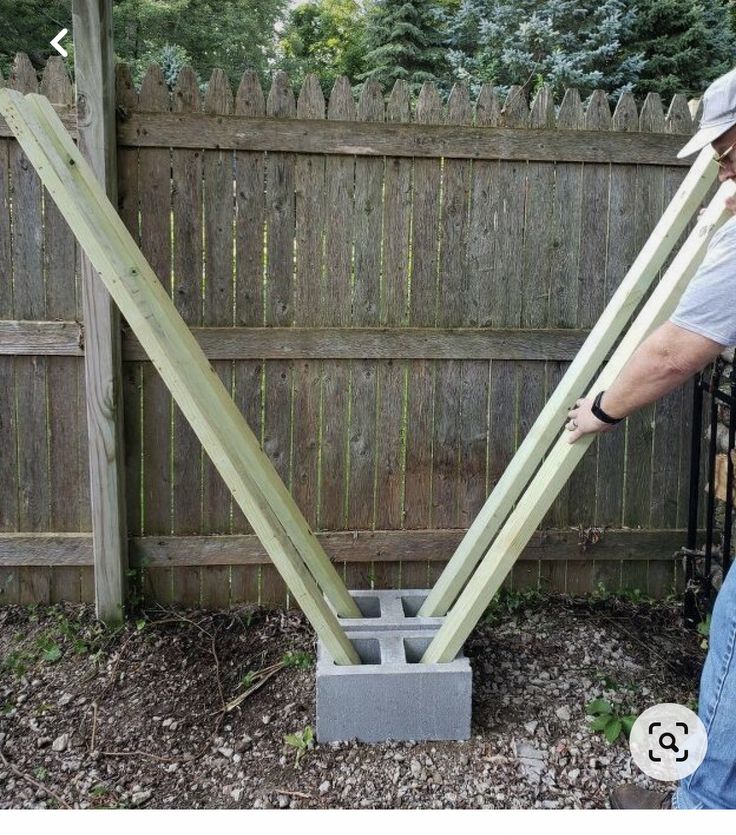 a man is holding two pieces of wood in front of a fence