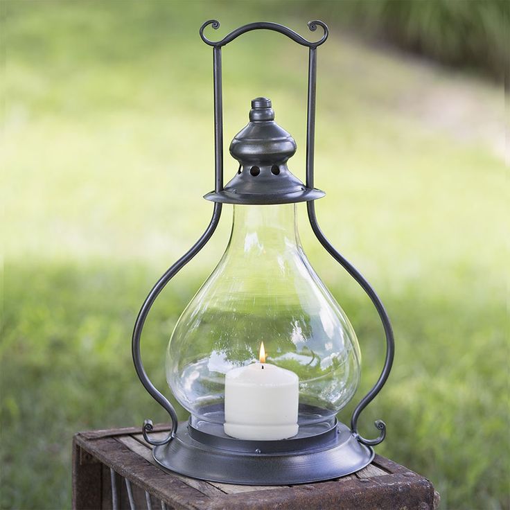 a candle is lit in a glass lantern on a wooden table outside with grass behind it