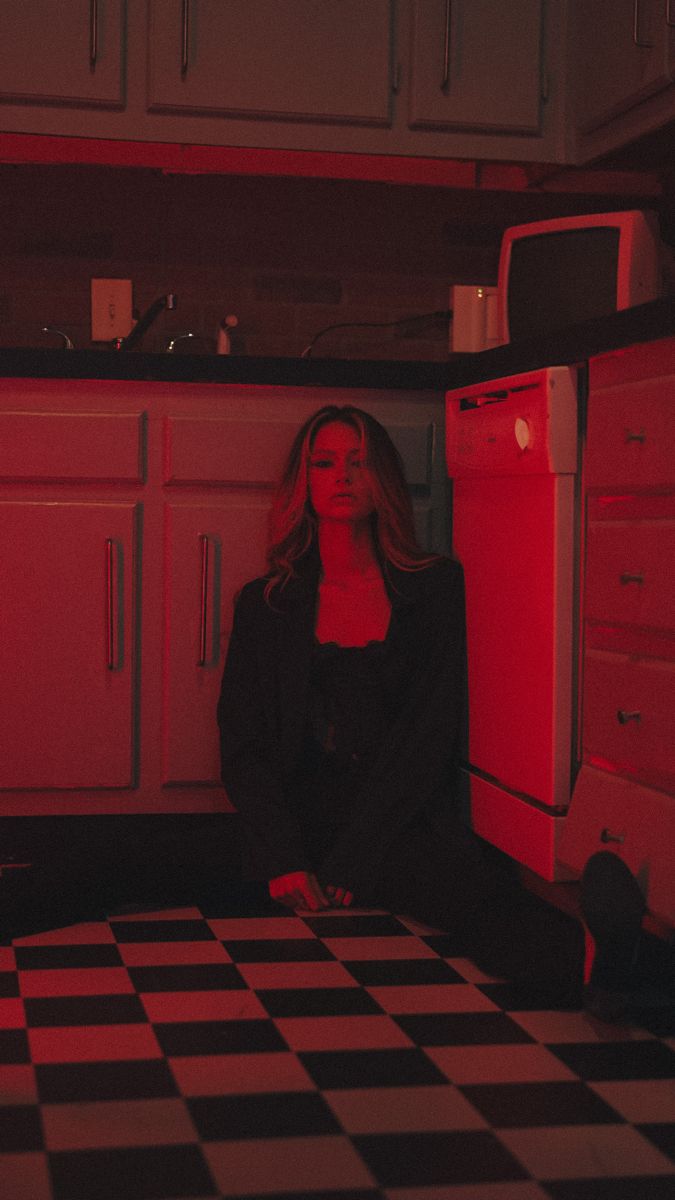 a woman sitting on the floor in a kitchen with red light coming from behind her