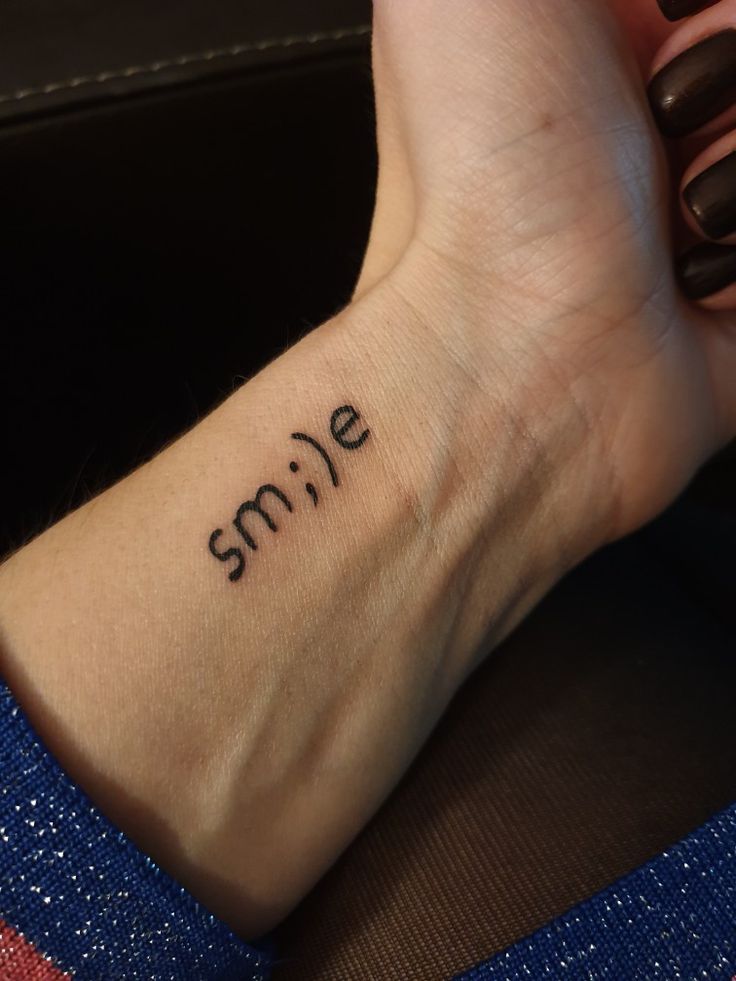 a woman's wrist tattoo with the word smile written on her left arm and hand