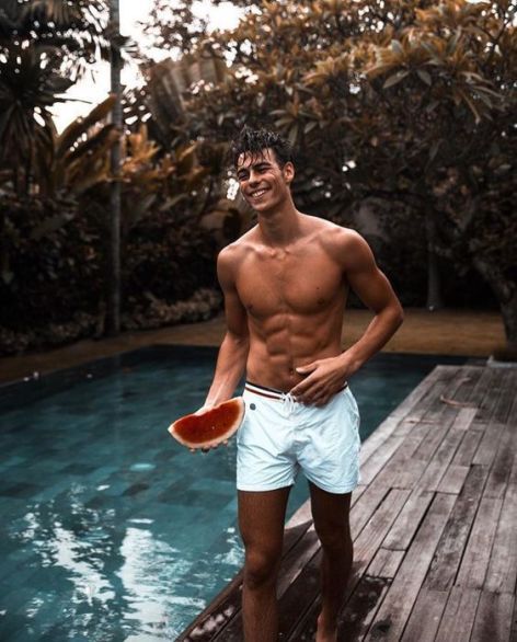 a man holding a frisbee standing next to a pool with trees in the background