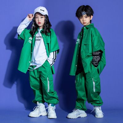 two children in green outfits standing next to each other against a blue wall, both wearing white sneakers