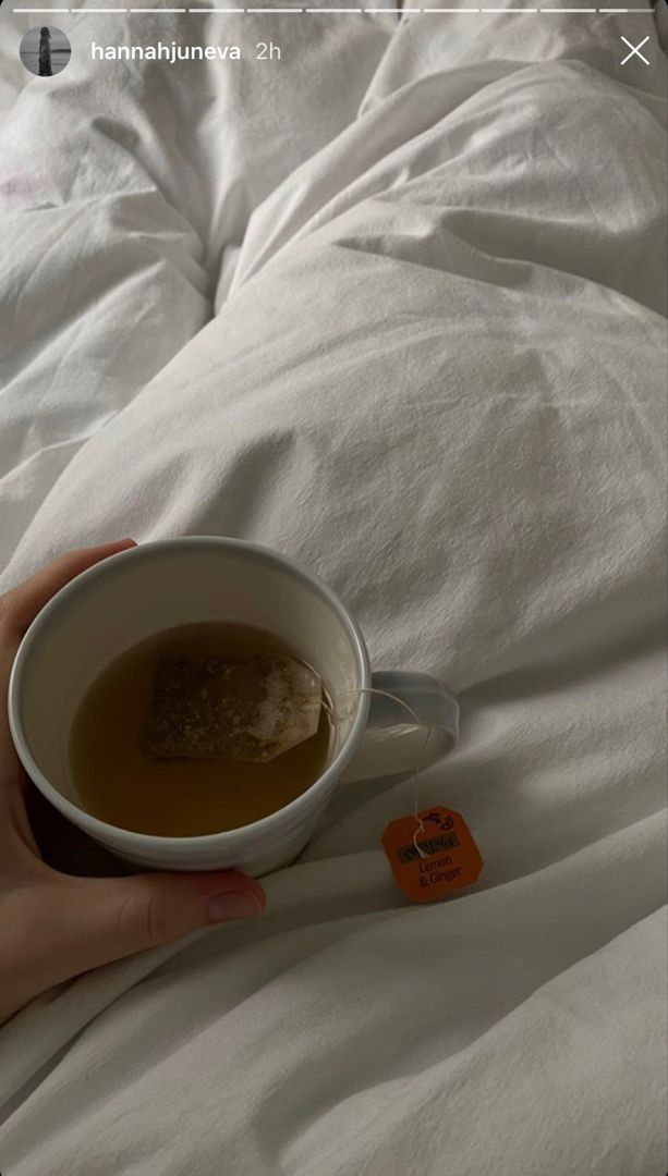 a person holding a cup of tea on top of a white bed covered in sheets