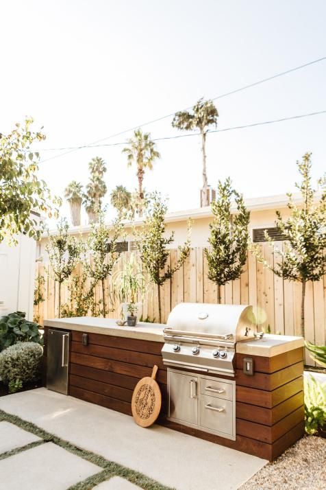 an outdoor kitchen with grill, sink and table in the middle of a backyard area