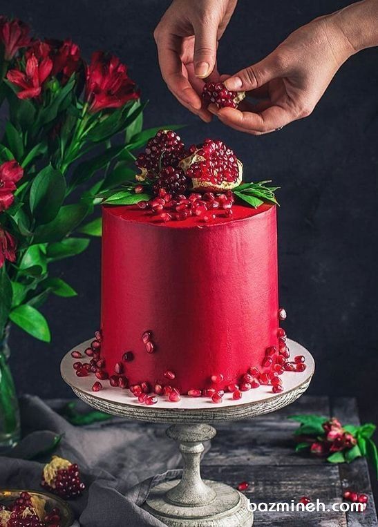 a woman is decorating a red cake with pomegranates